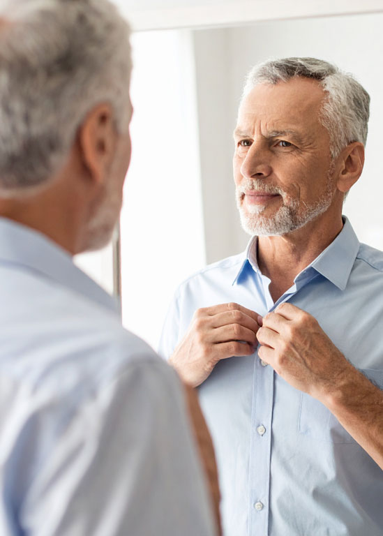 Comprendre-opt Homme âgé ajustant sa chemise devant le miroir.