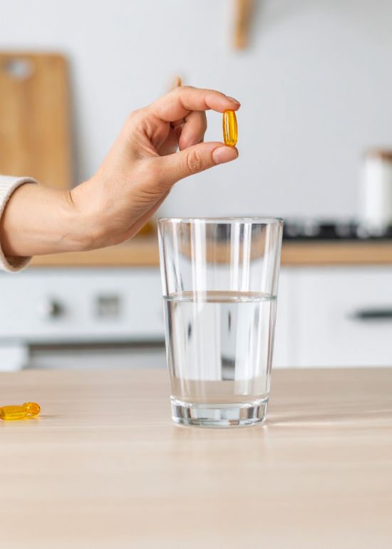 Medicaments Main tenant une gélule au-dessus d'un verre d'eau.
