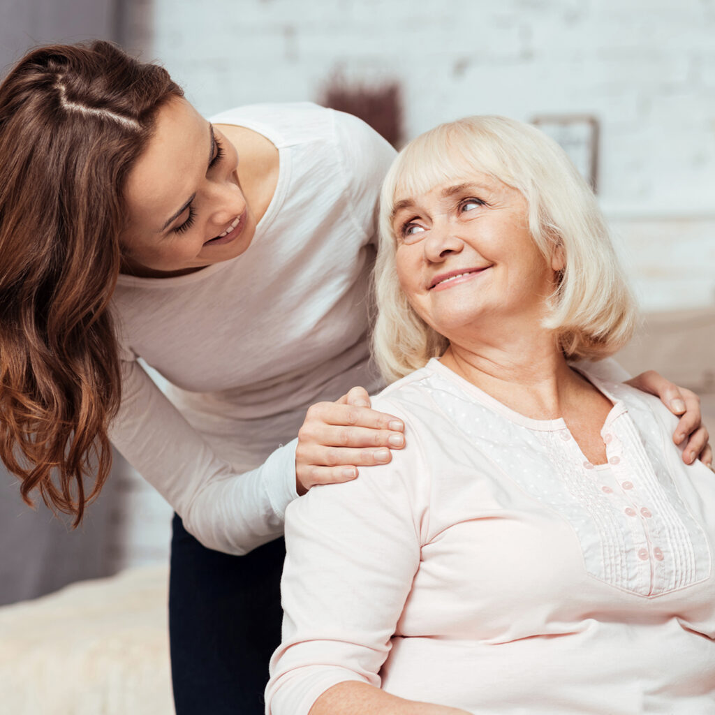 Cheerful woman taking care of her grandmother in wheelchair Femme souriante interagissant avec une senior bienveillante.