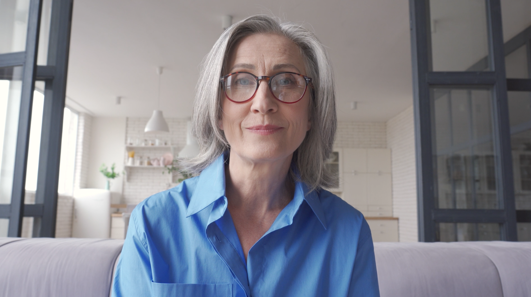 Capture d’écran 2025-07-23 à 18.36.50 Femme souriante avec des lunettes dans un intérieur.