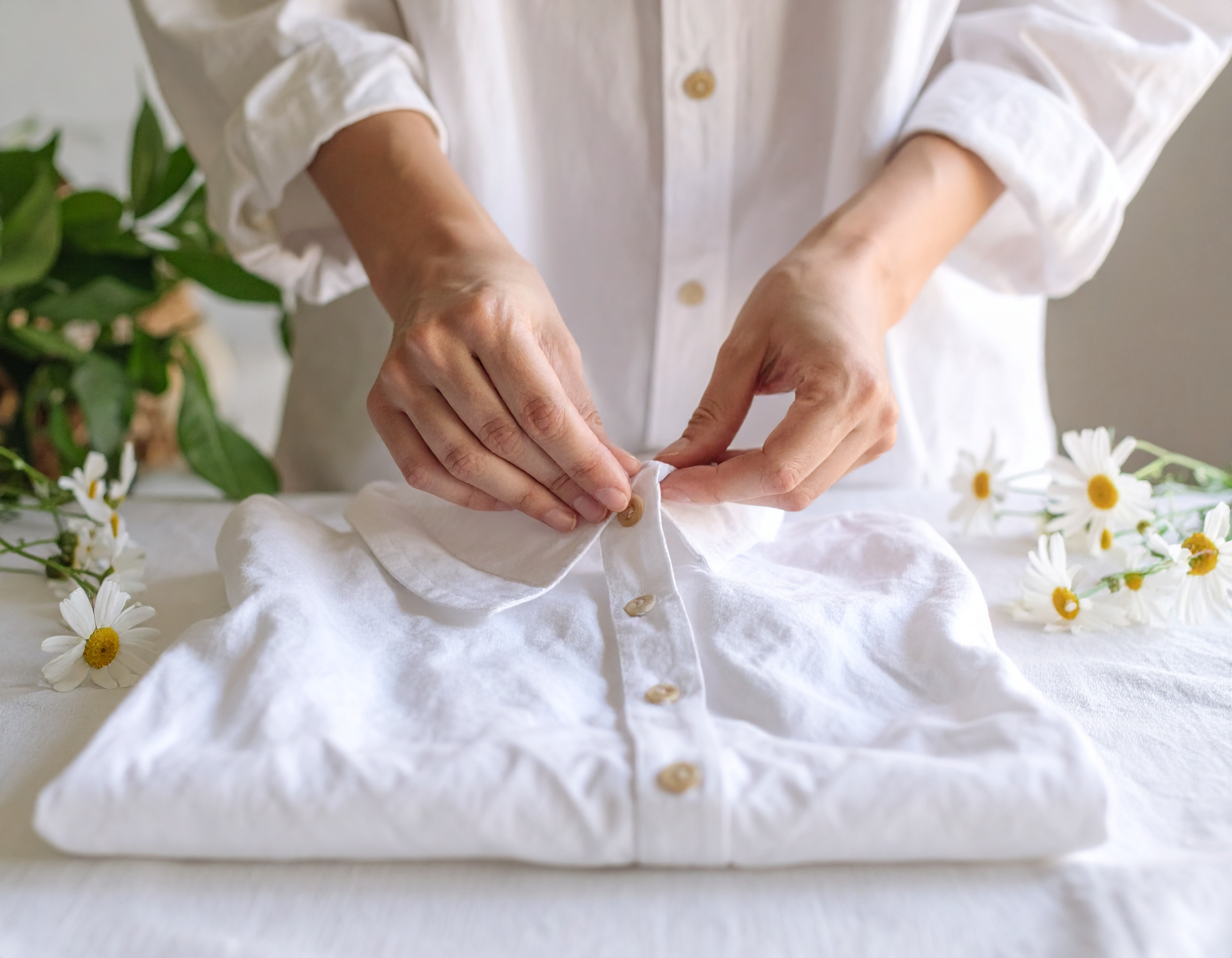 Firefly_Photo ultra réaliste d’une main féminine en train de boutonner une chemise ou cuisine 648595 Femme plie une chemise blanche avec des fleurs.