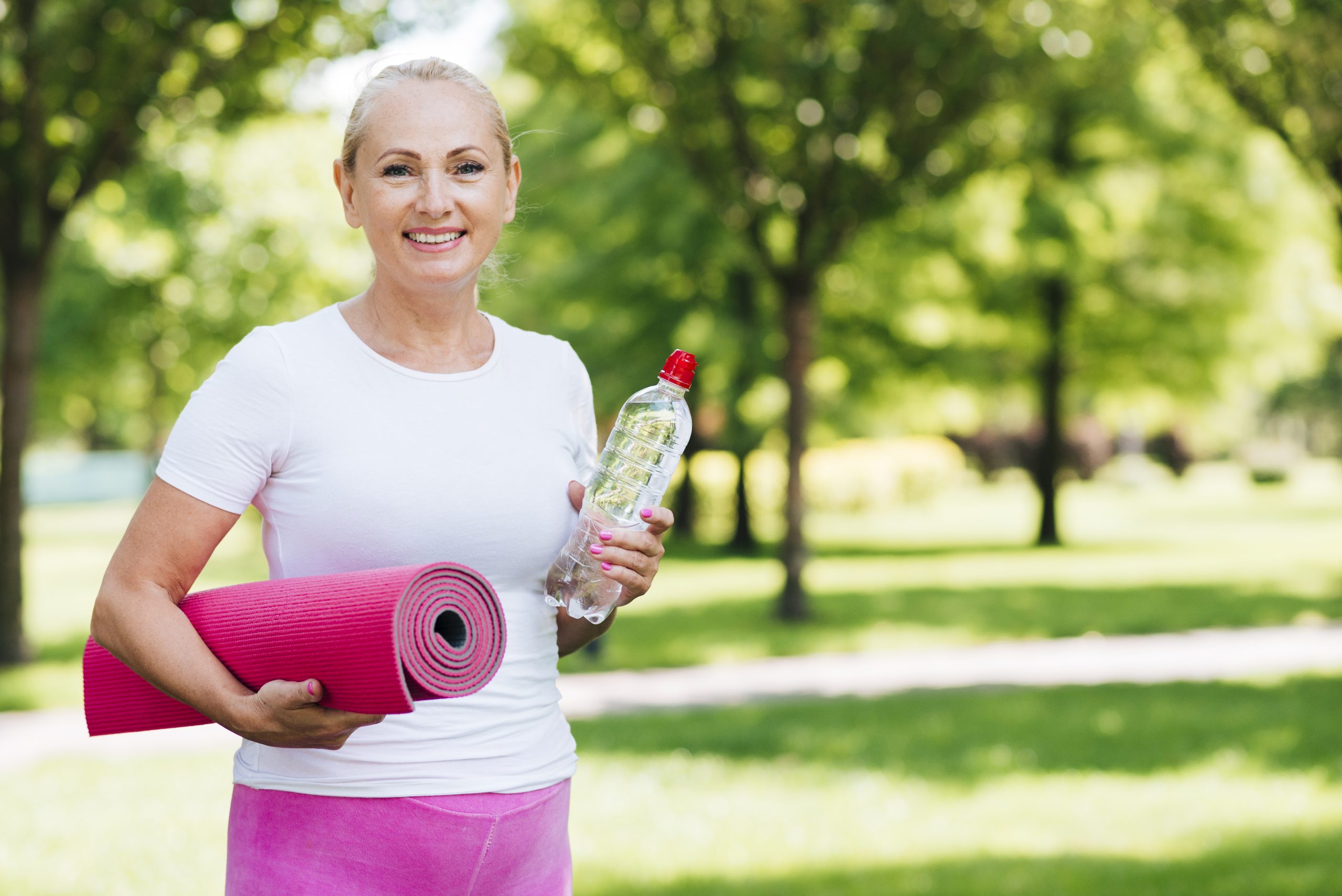 Femme souriante avec tapis de yoga et bouteille d'eau